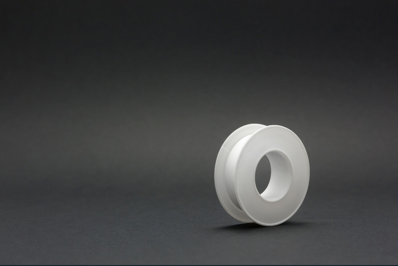 A roll of teflon tape in a dark grey background used to represent its use in secruring laptop screws